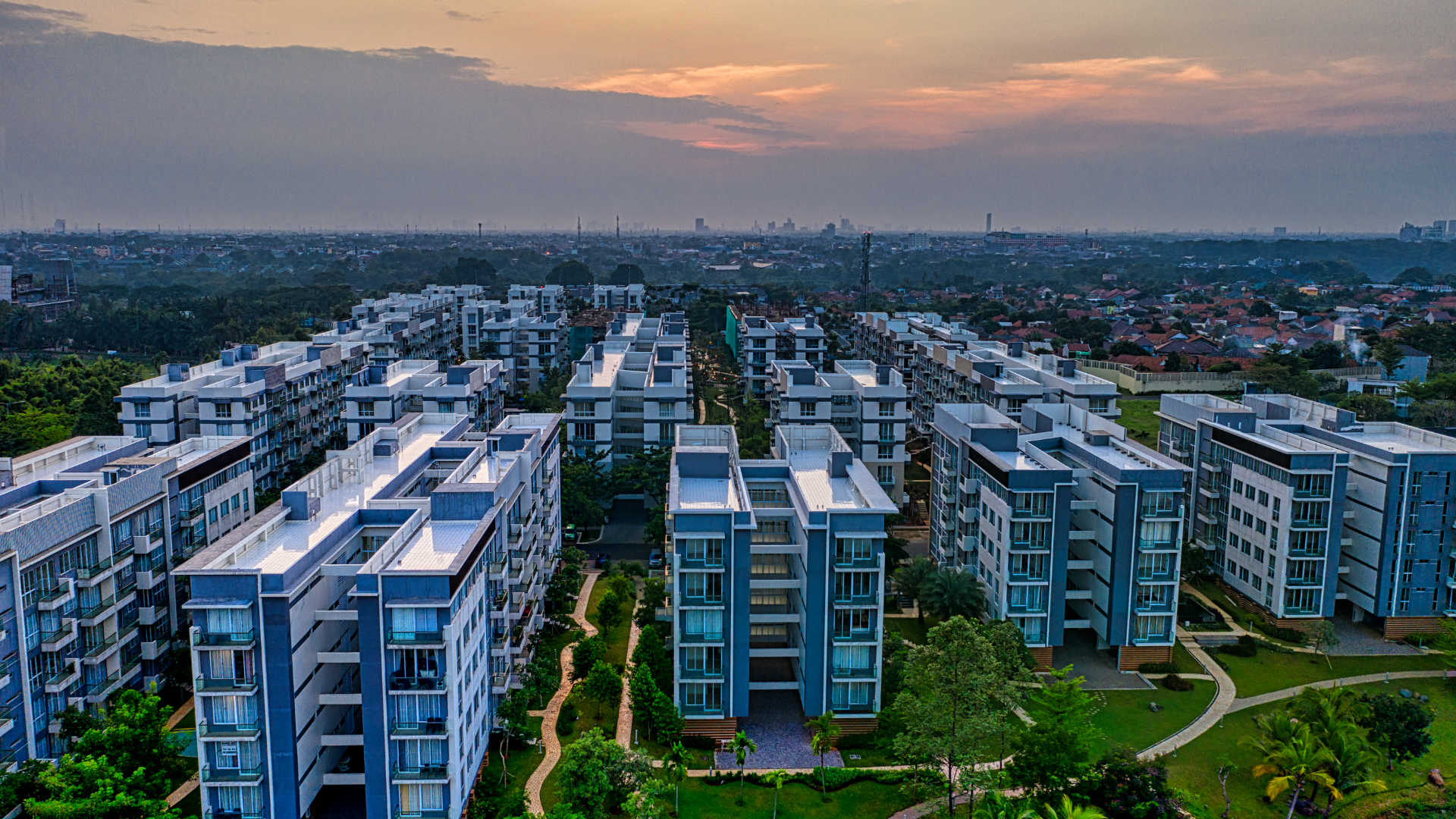Vista aérea de edificios residenciales y jardines al atardecer.